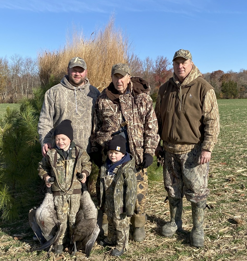 Three men and two children pose for a photo in hunting gear with two geese they shot.