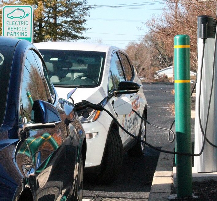 Two cars parked at, and using, an electric vehicle charger.