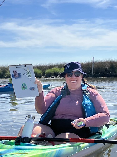 A woman in a kayak holding up a painting. 